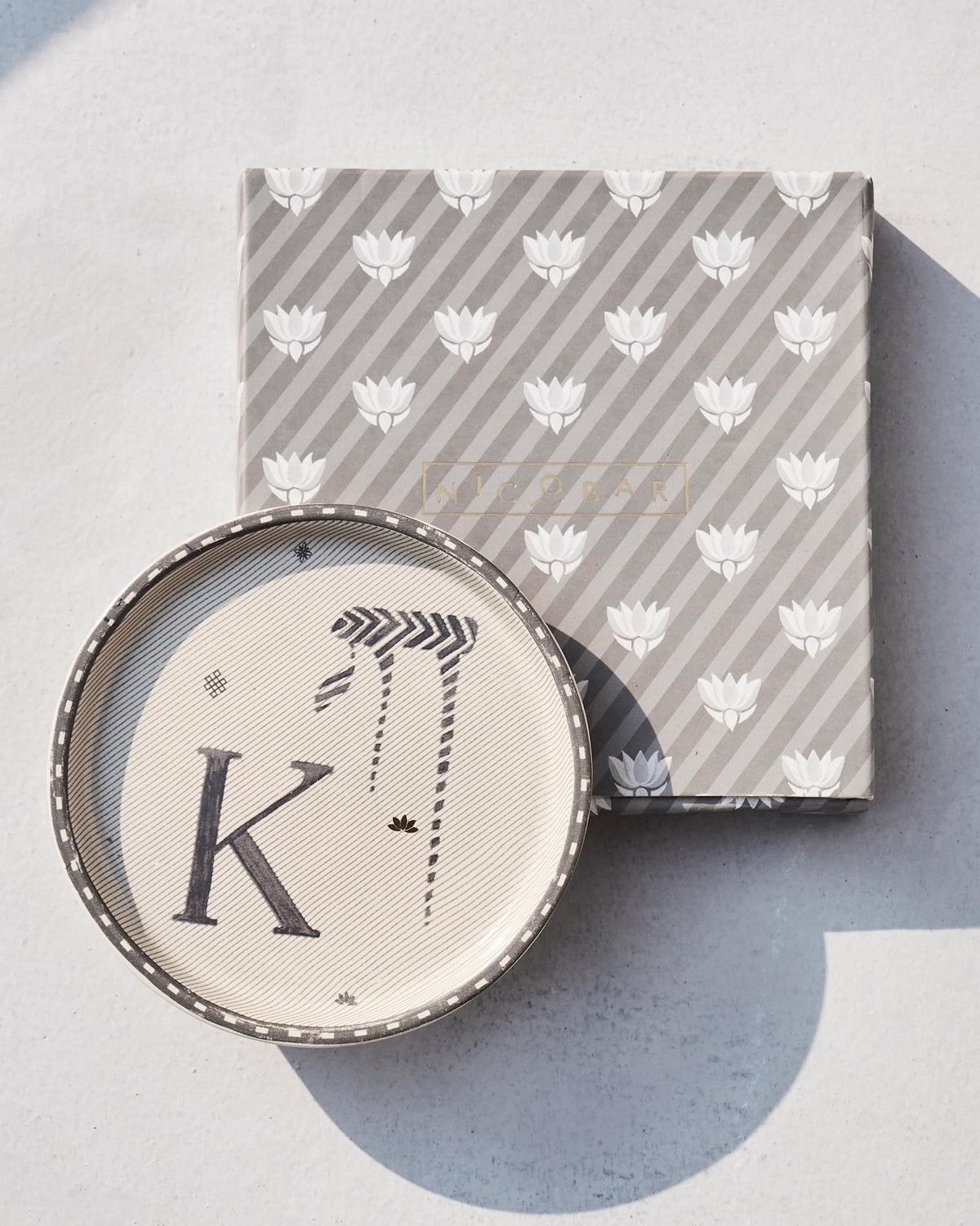 Akshar Coaster with a letter K resting on its lotus-print gift box.