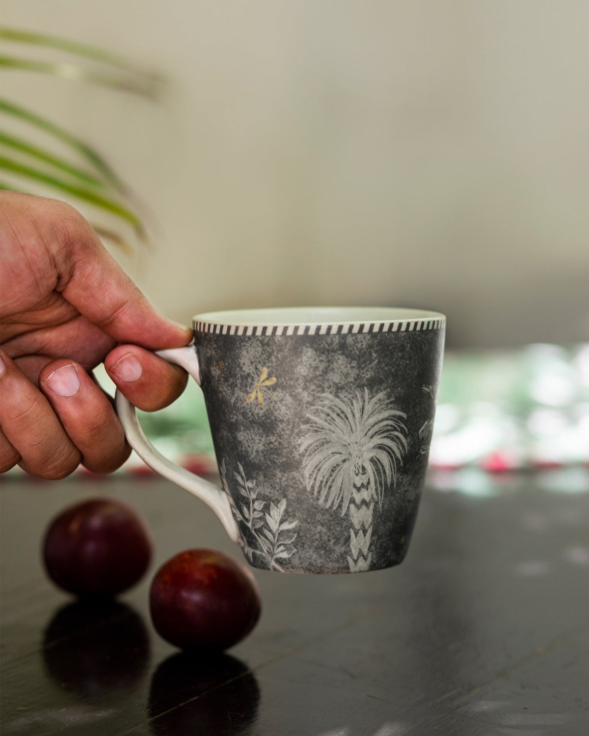 Periyar Mug Charcoal held in a hand, showing a palm tree motif.