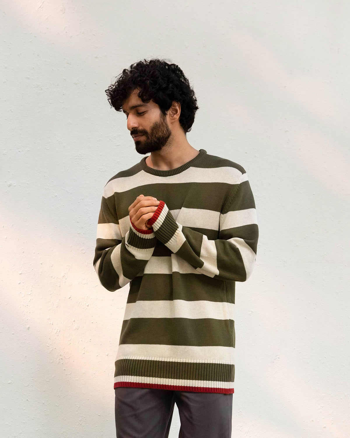Person wearing a striped olive and oatmeal Round Neck Sweater with red cuffs.