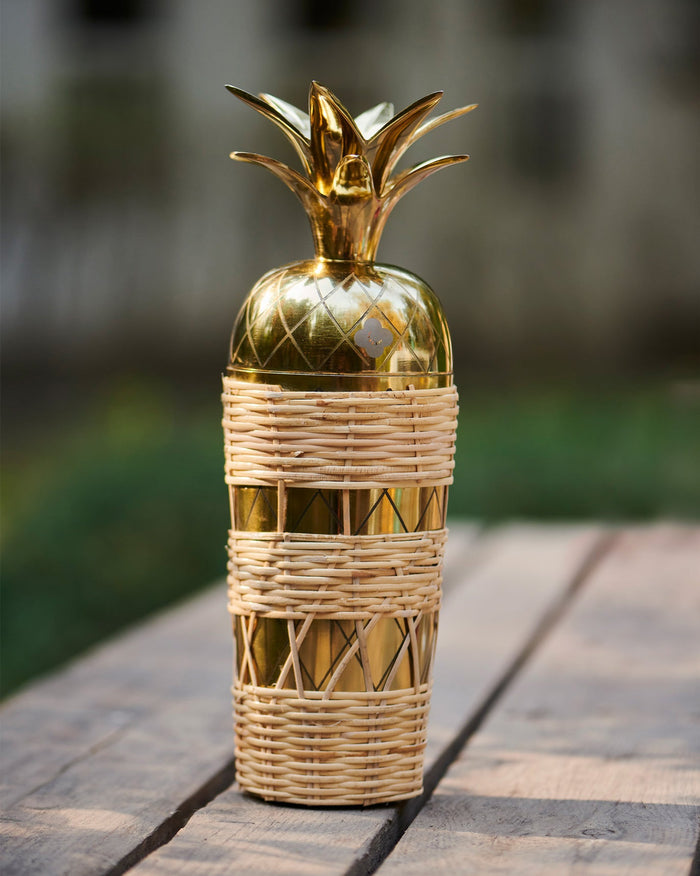 Ananasi cocktail shaker shaped like a gold pineapple with a woven outer sleeve.