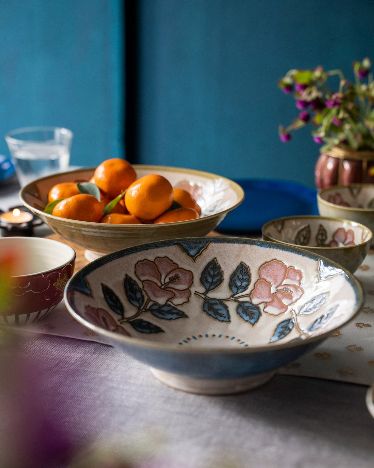 Moor Shallow Bowl with pink flowers and blue leaves, set on a table.