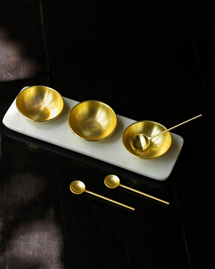 Dariya Tray Set with three gold brass bowls and spoons on a marble tray.
