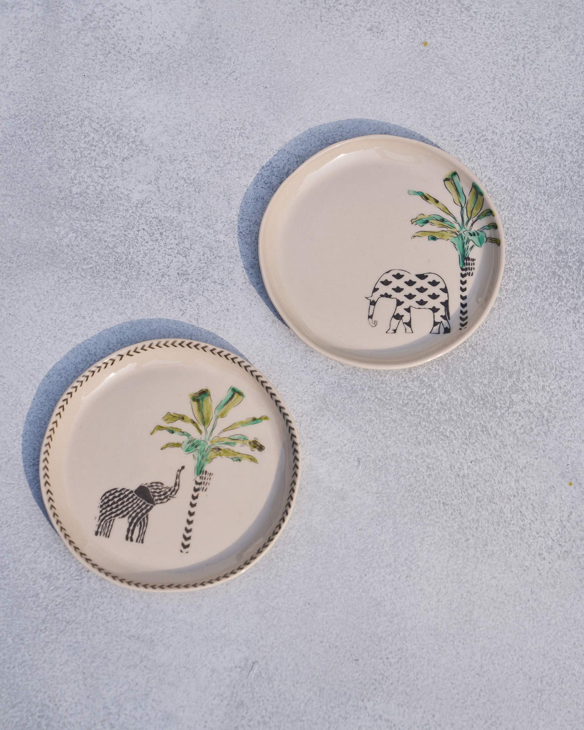 Two ivory coastal tea plates with black elephants, green palms, and a chevron rim.