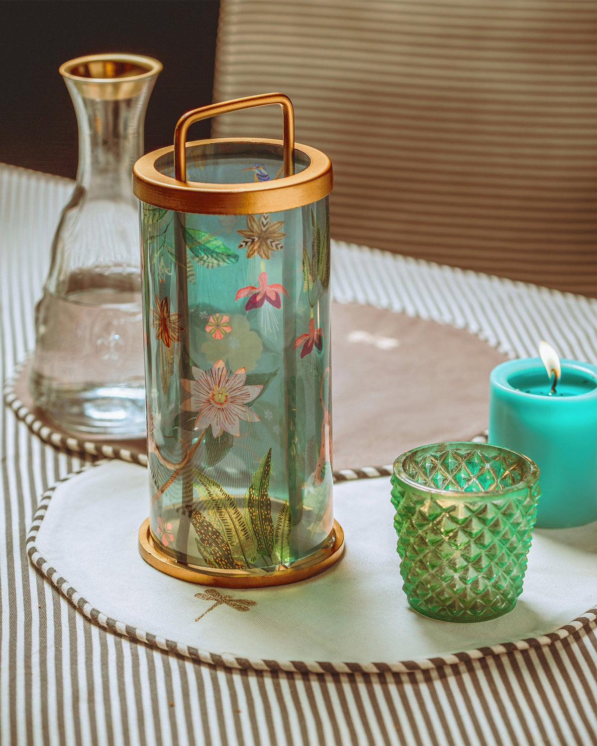 Cirrus Lantern beside a green glass votive holder and a teal candle.