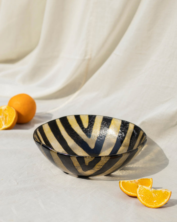 Dariya Bowl Large with black and gold stripes on a white cloth.