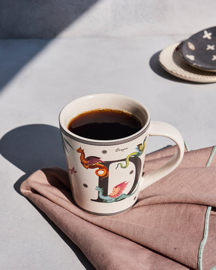 Cream Dariya mug with a letter D and dragon motifs, filled with coffee.