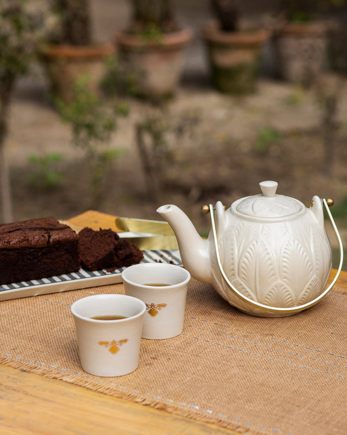 Teesta teapot and teacups with bee motifs beside cake.