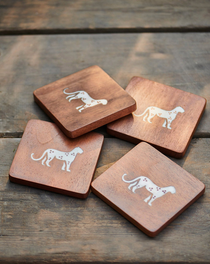 Four square coasters, each with a white cheetah motif.