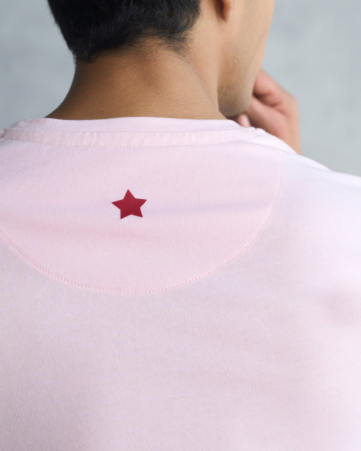 Close-up of a soft pink t-shirt showing a small red star at the back neckline.