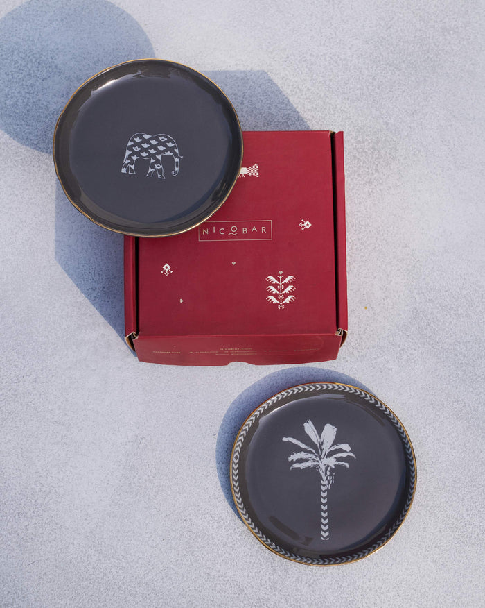 Pair of Coastal Tea Plates in charcoal, one with an elephant and one with a palm motif, shown with a Nicobar box.