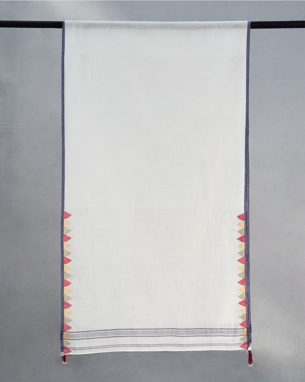 White Cara Scarf hung on a rod, showing its triangle border at both ends.