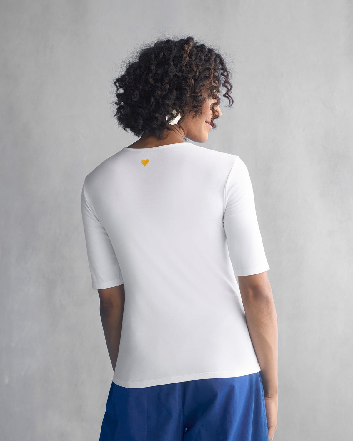 Back of a white Luna Jersey Top with a small yellow heart at the neck.