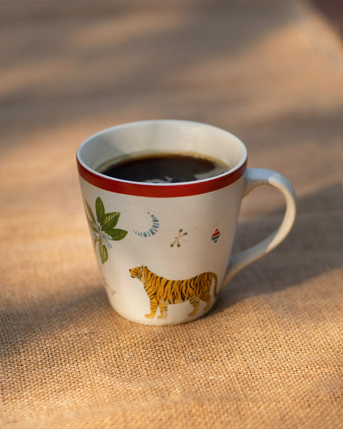 Cream Nadi conical mug with a red rim and orange tiger print, filled with coffee.