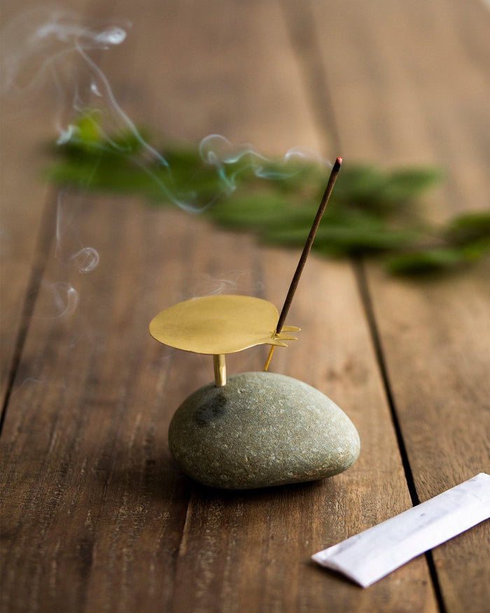 Pebble incense holder with a gold disc on a grey stone, holding an incense stick.