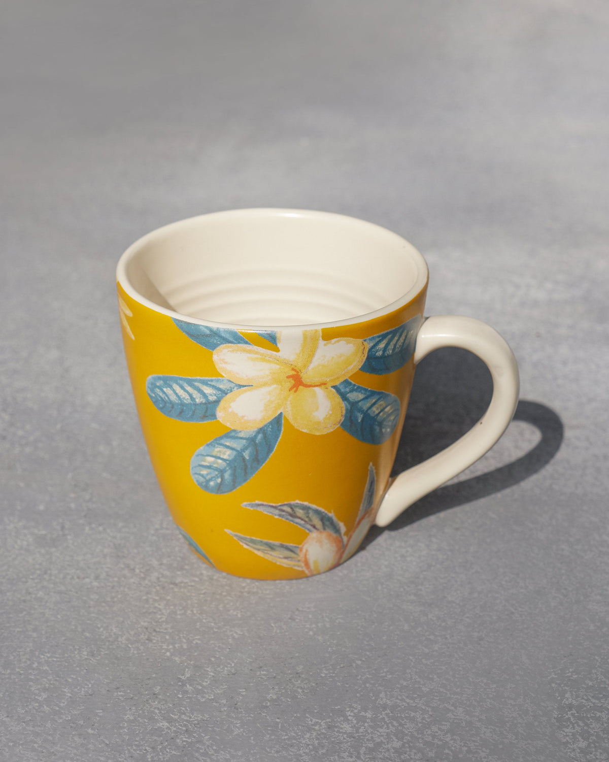 Angled view of the Champa Mug in yellow, with flowers on the side.