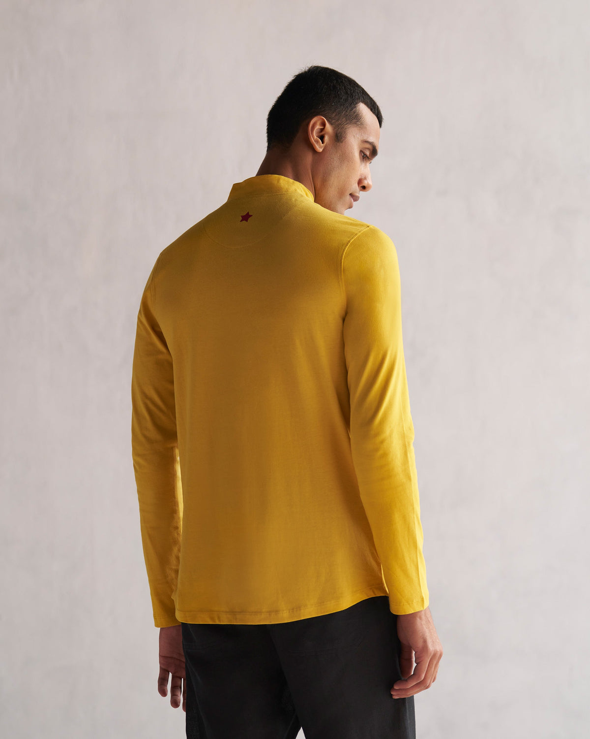 Back of a mustard turtle neck t-shirt worn by a person.