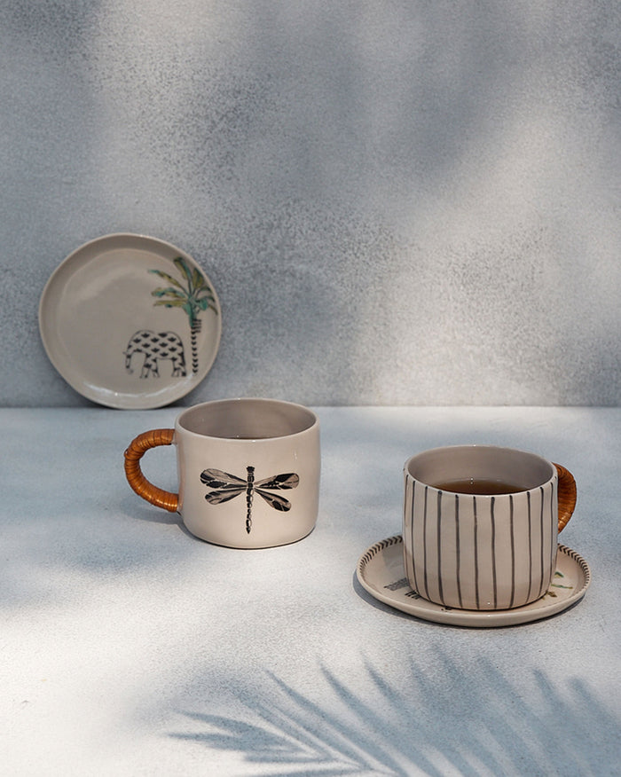 Cream dragonfly and striped mugs with cane-wrapped handles on a table.