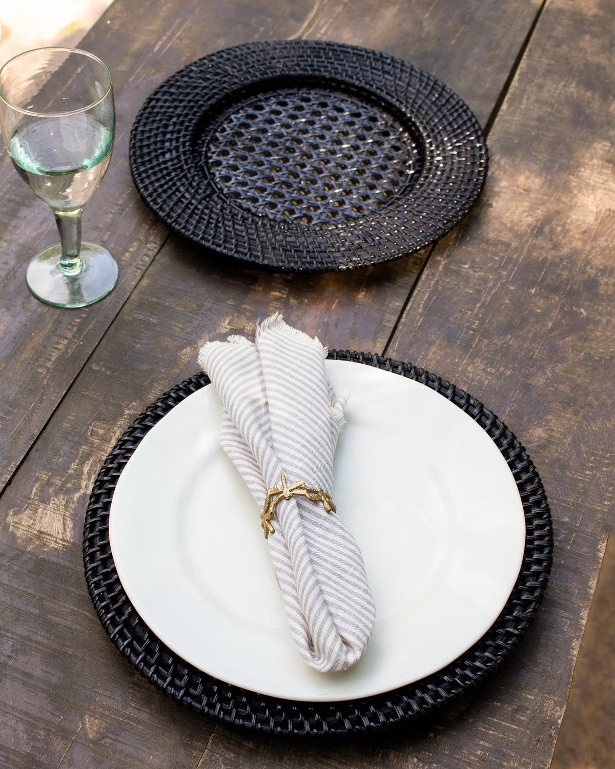 Black Rattan Charger placed under a white plate on a table.