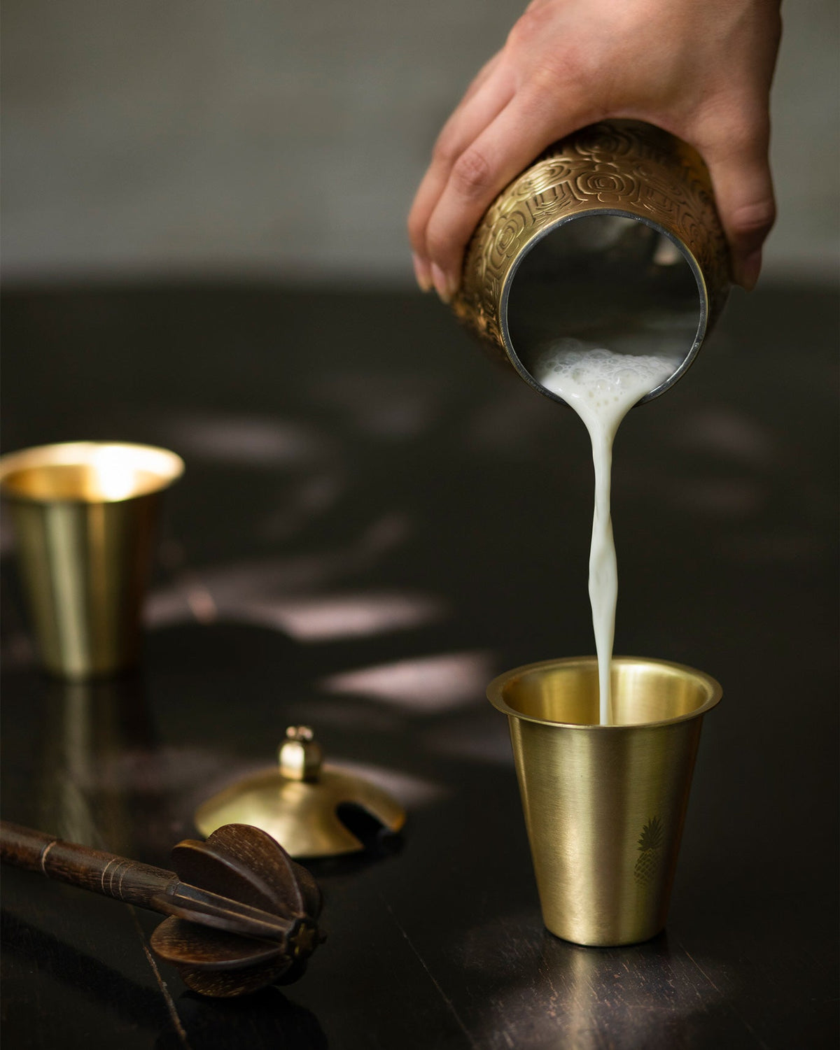 Hand pouring milk from a brass jug into a Dariya Tumbler.