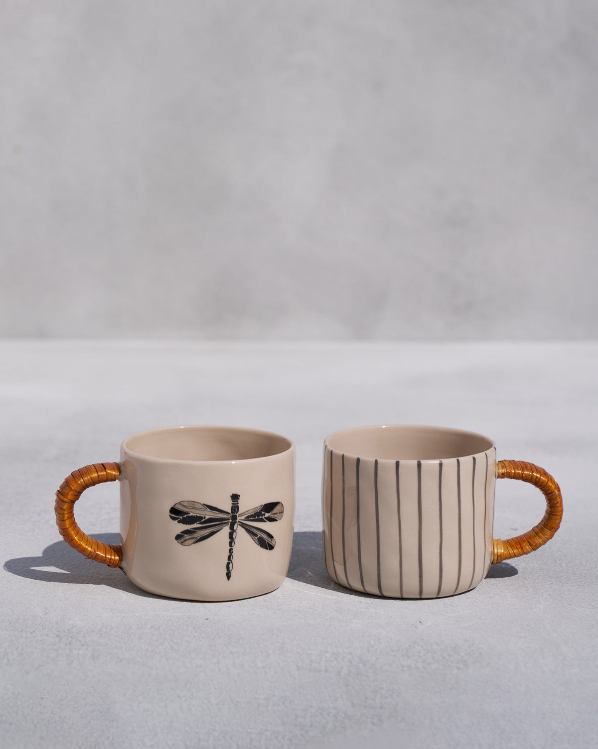 Pair of cream mugs with a dragonfly print and stripes, both with cane handles.