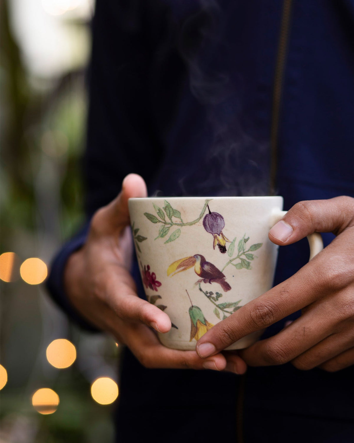 Person holding a Nakano mug with birds and leafy branches.