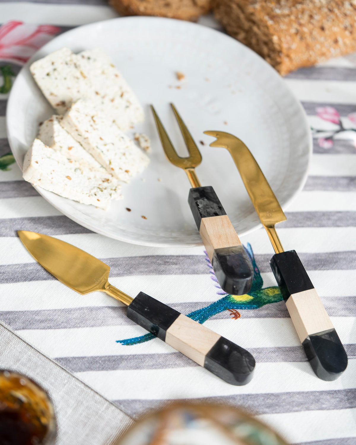 Celeste Cheese Knives (Set of 3) on a striped table beside a plate.