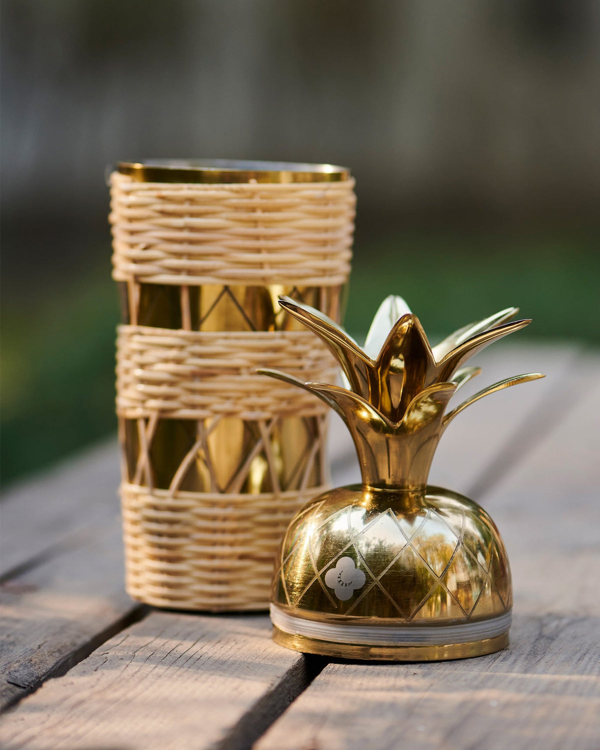 Ananasi cocktail shaker with its woven body beside the gold pineapple top.