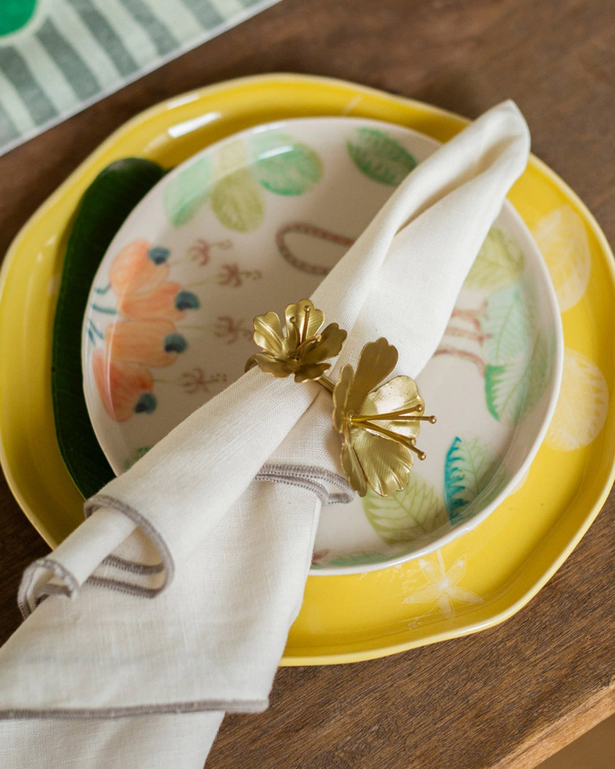 Gold floral napkin ring from the Jungle Table Set on stacked dinner plates.