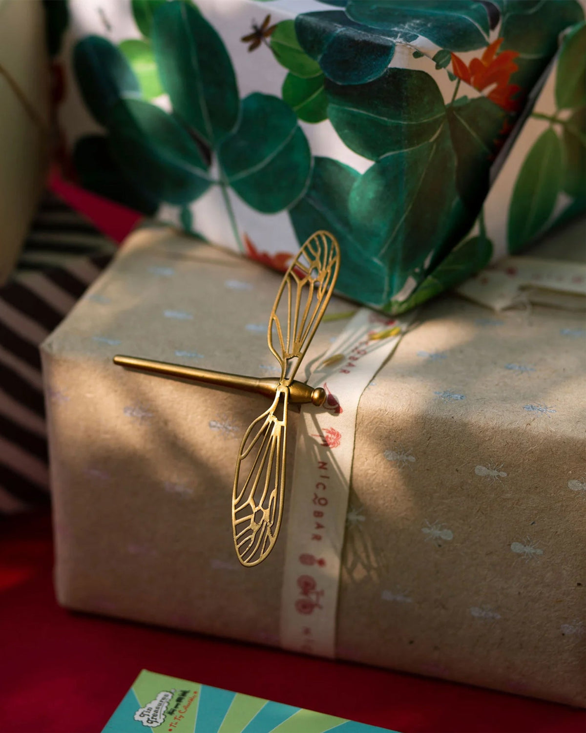 Dragonfly accent piece in gold resting on a kraft-wrapped gift with a Nicobar ribbon.