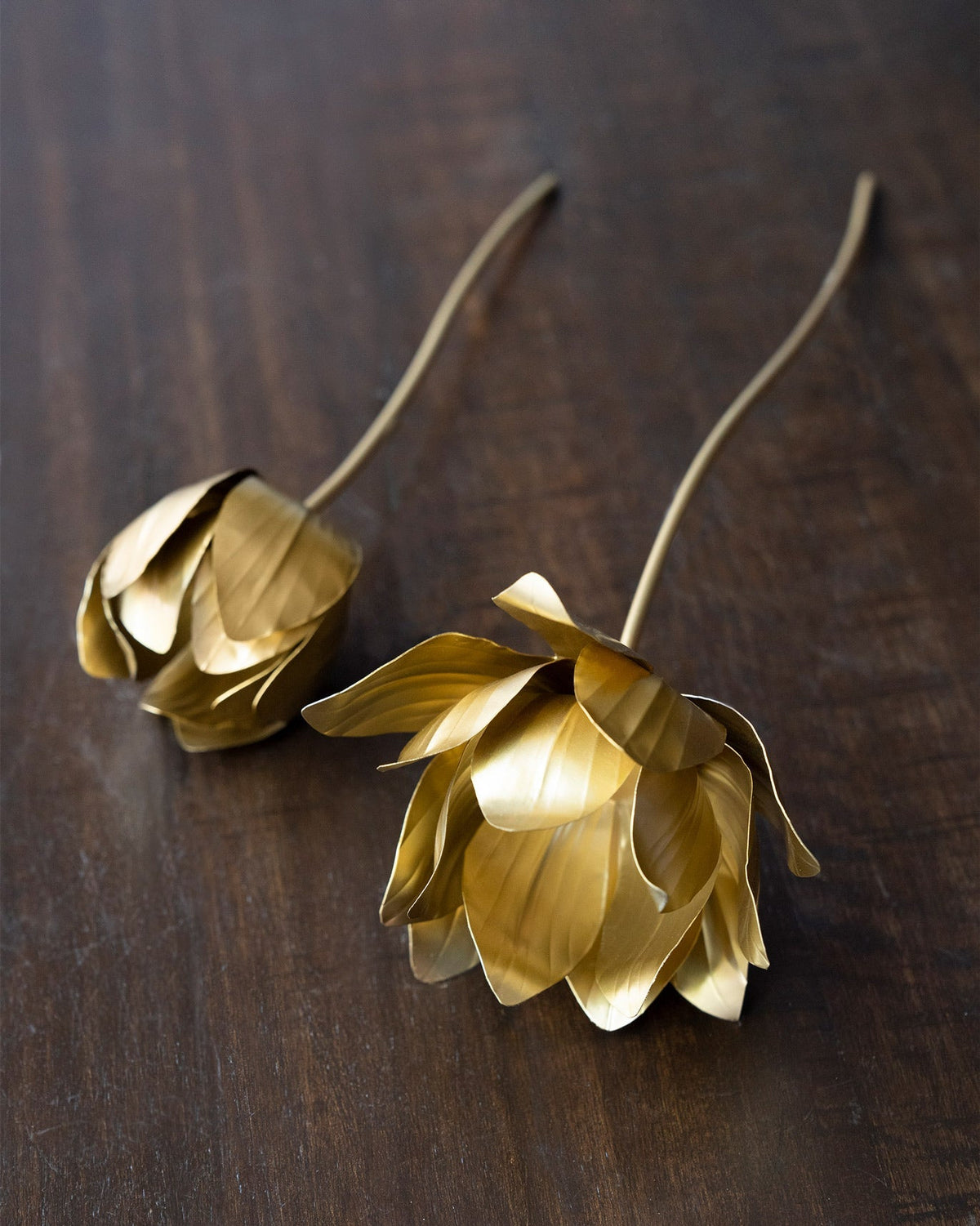 Kamal Accent Piece gold metal lotus flowers with curved stems lying on a wooden table.