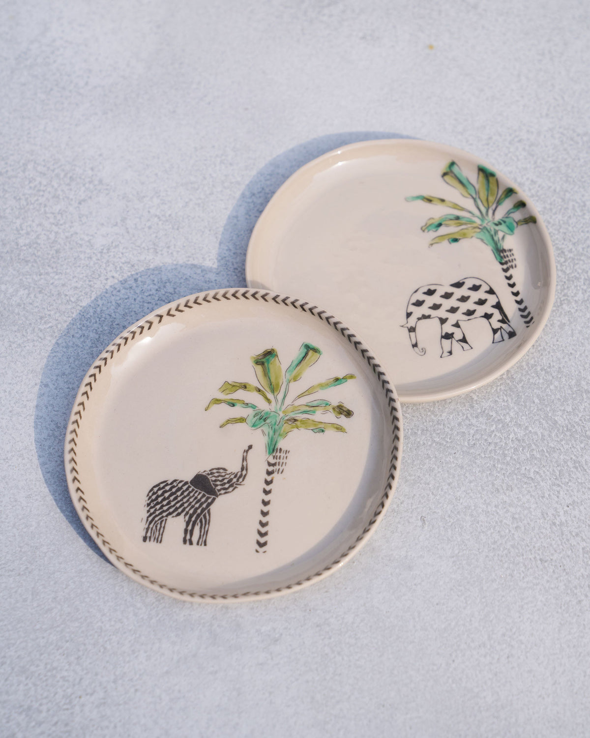 Ivory coastal tea plates showing two elephant-and-palm designs side by side.