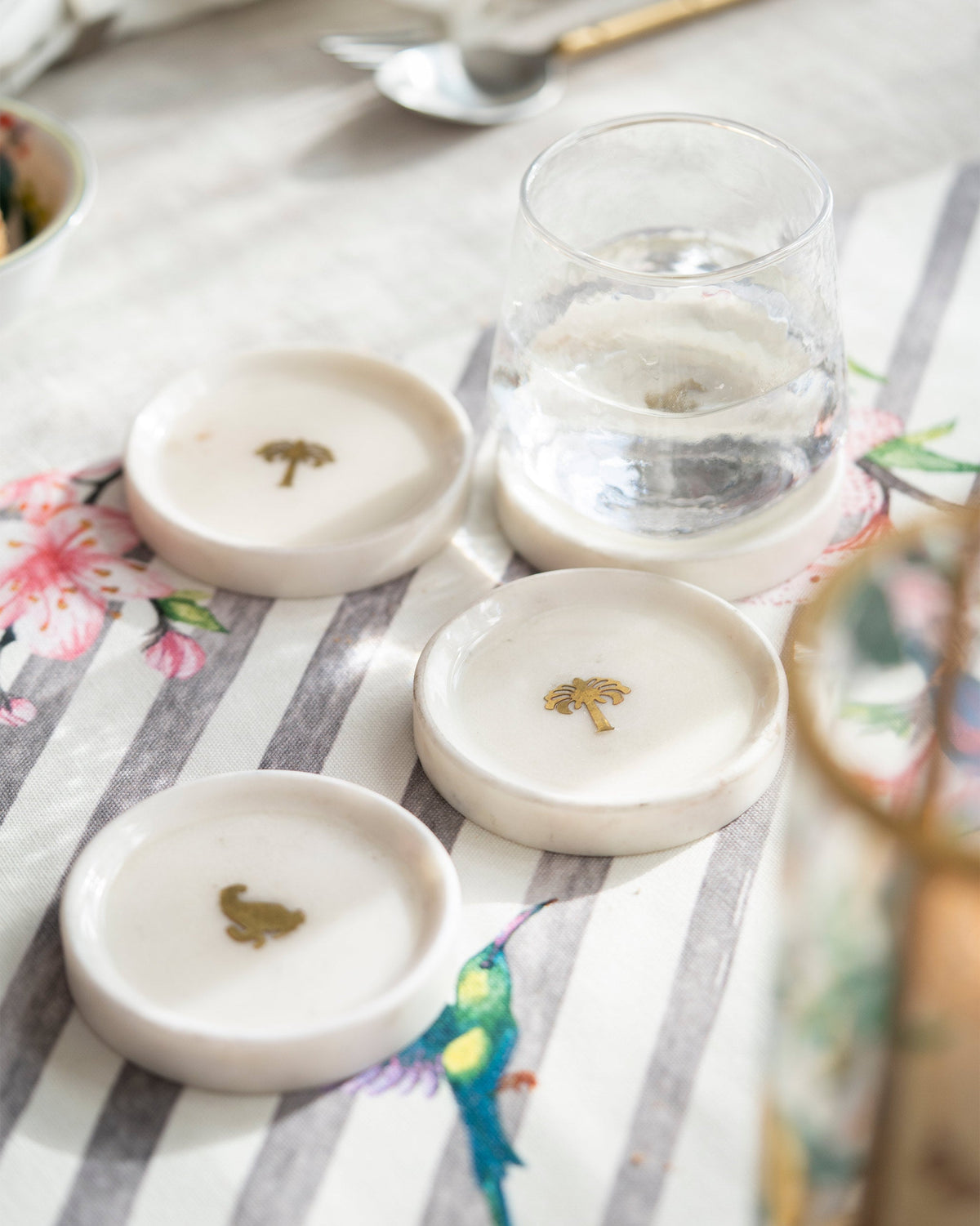 Celeste Coasters (Set of 4) with gold motifs beside a glass of water.