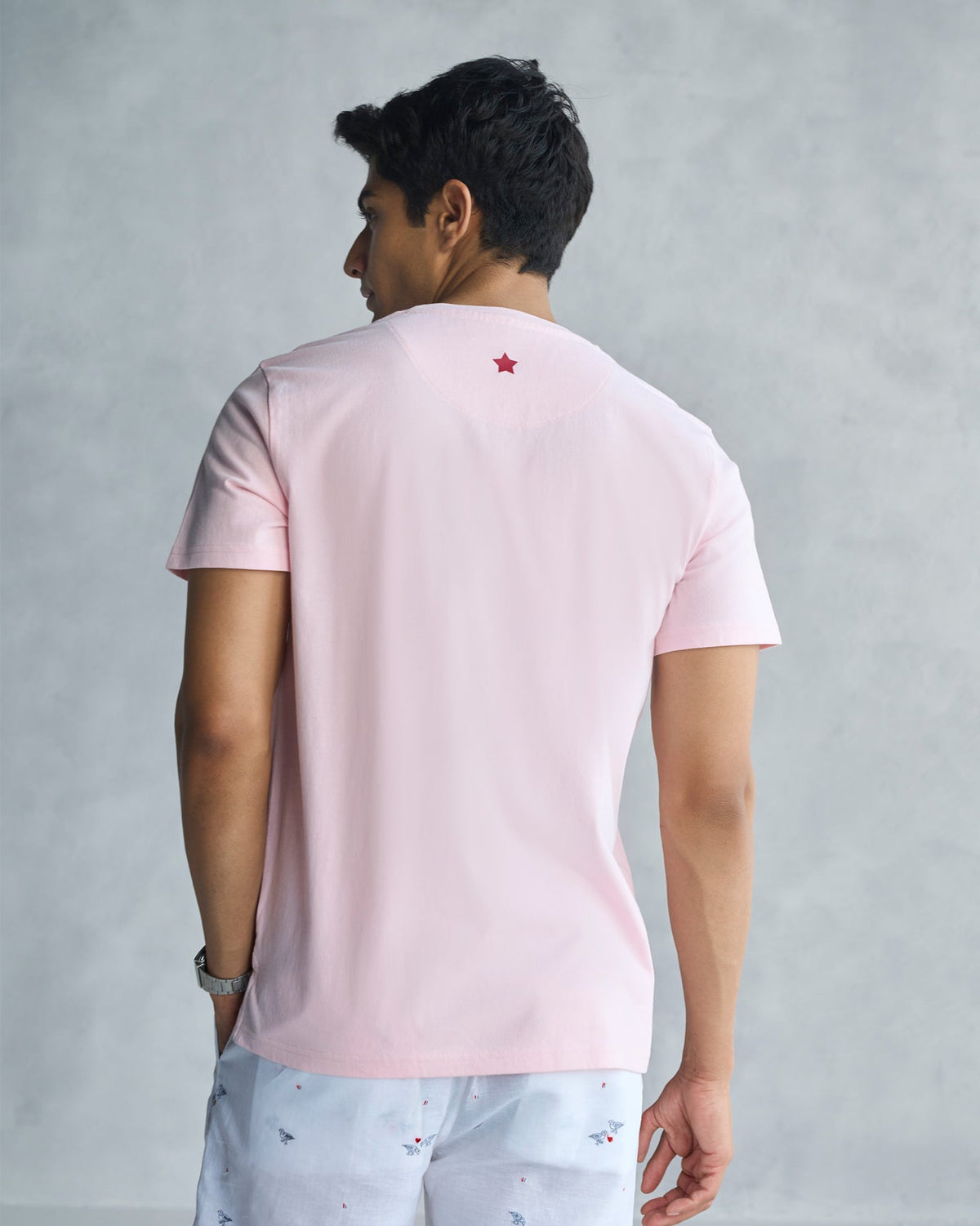 Back of a soft pink See Ya Later Alligator t-shirt with a small red star worn by a person.
