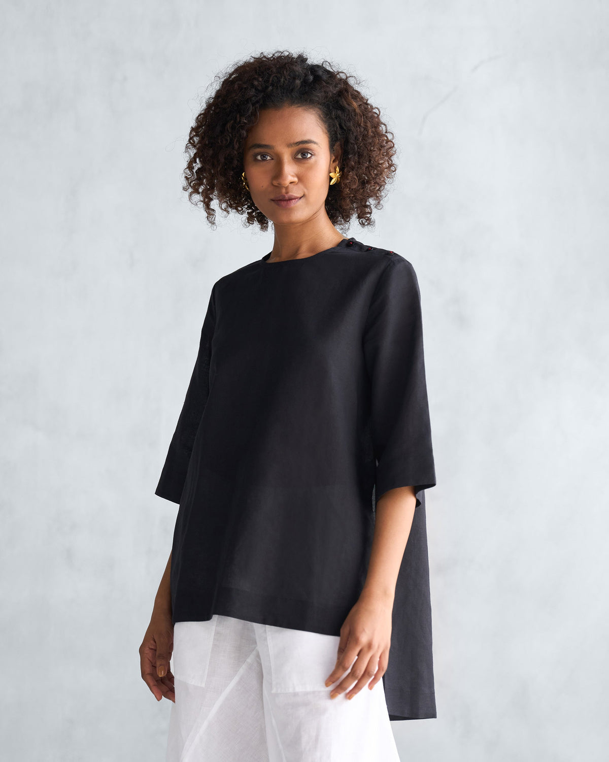 Black High Slit Top showing a longer back hem over white pants.