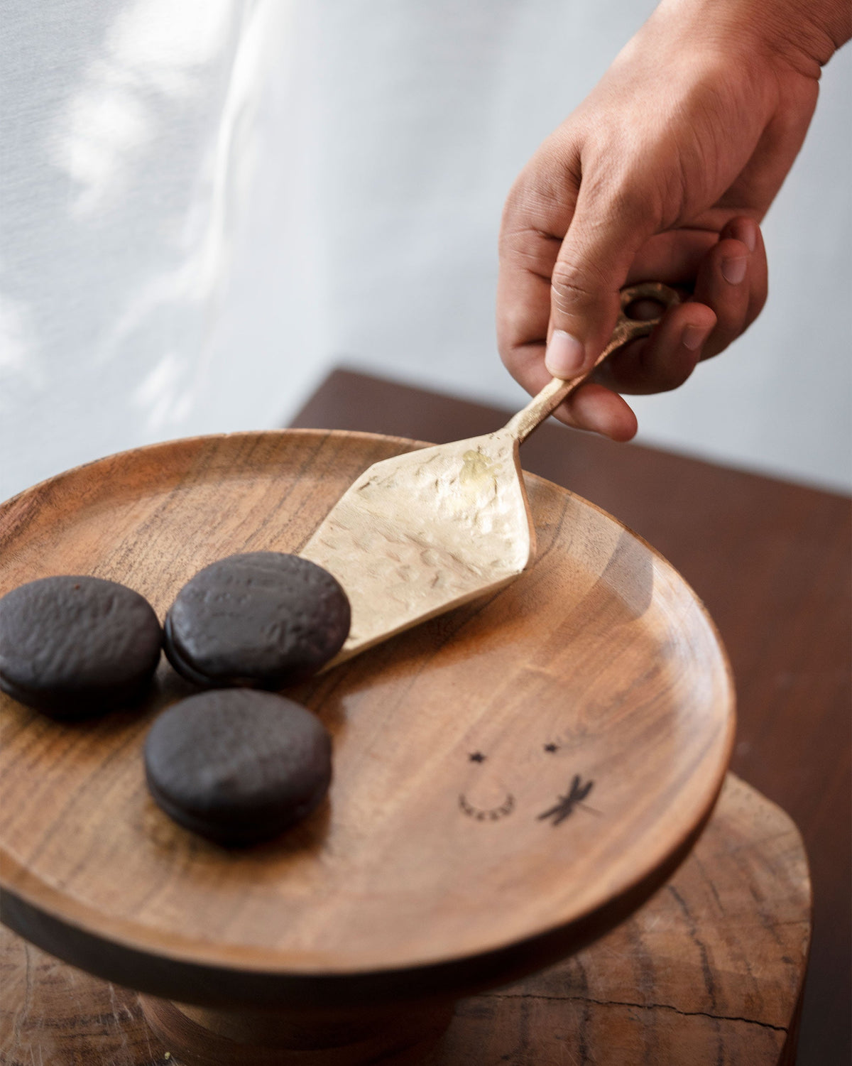 Celeste Spatula held over dark round cookies on a wooden plate.