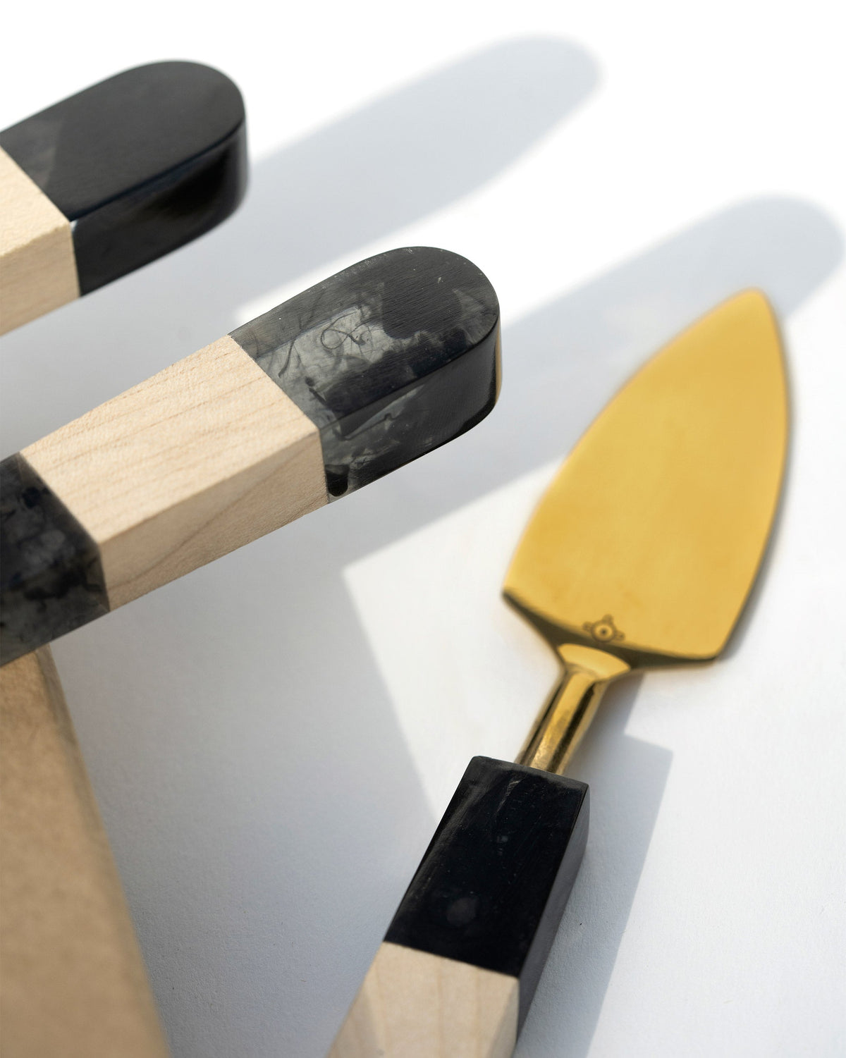 Close-up of Celeste Cheese Knives showing a gold spatula and black and wood handle.