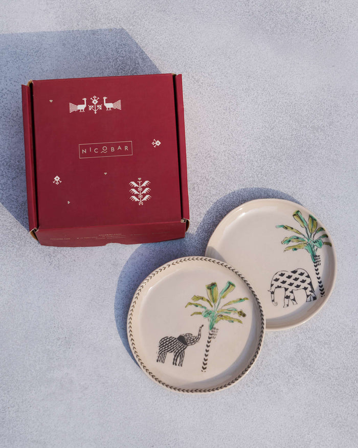 Ivory coastal tea plates with elephant and palm motifs beside a red gift box.