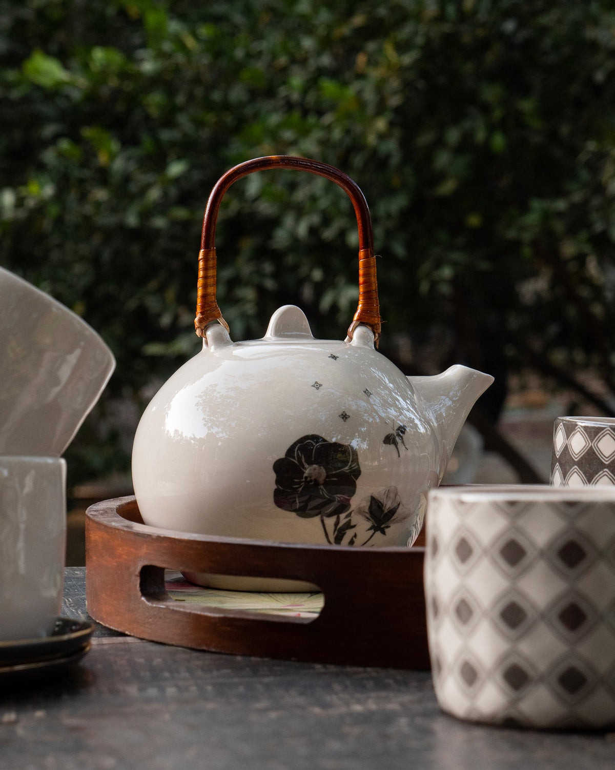 Poppy teapot on a round wooden tray with cups in a garden setting.