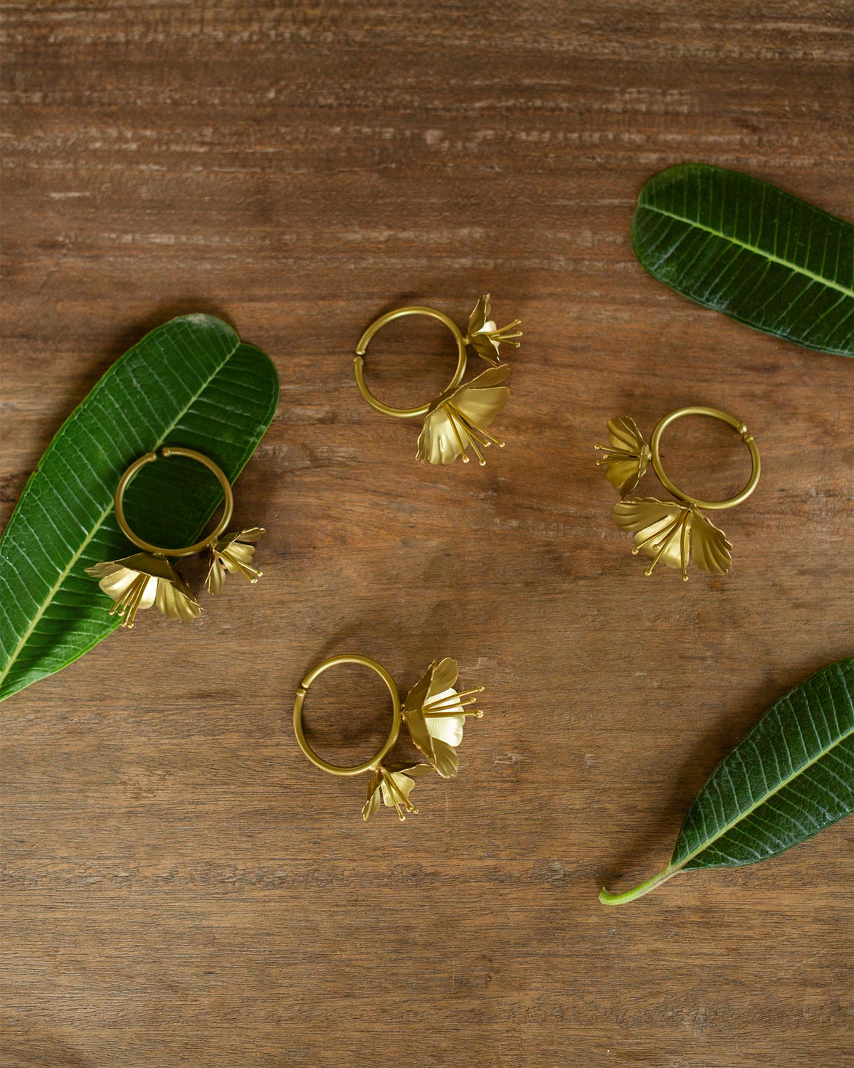 Four gold floral napkin rings from the Jungle Table Set on dark wood.