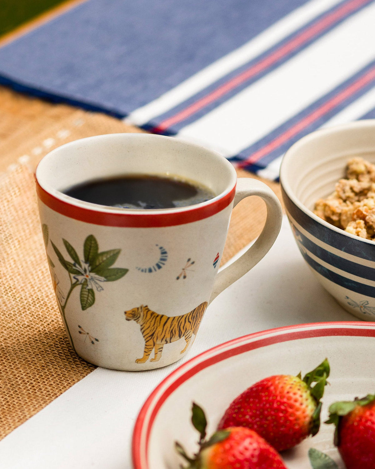 Nadi conical mug with tiger print set beside a matching red-rim breakfast plate.