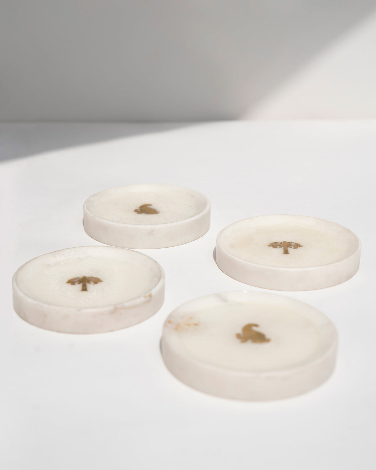 Angled view of Celeste Coasters (Set of 4) with gold motifs on white.