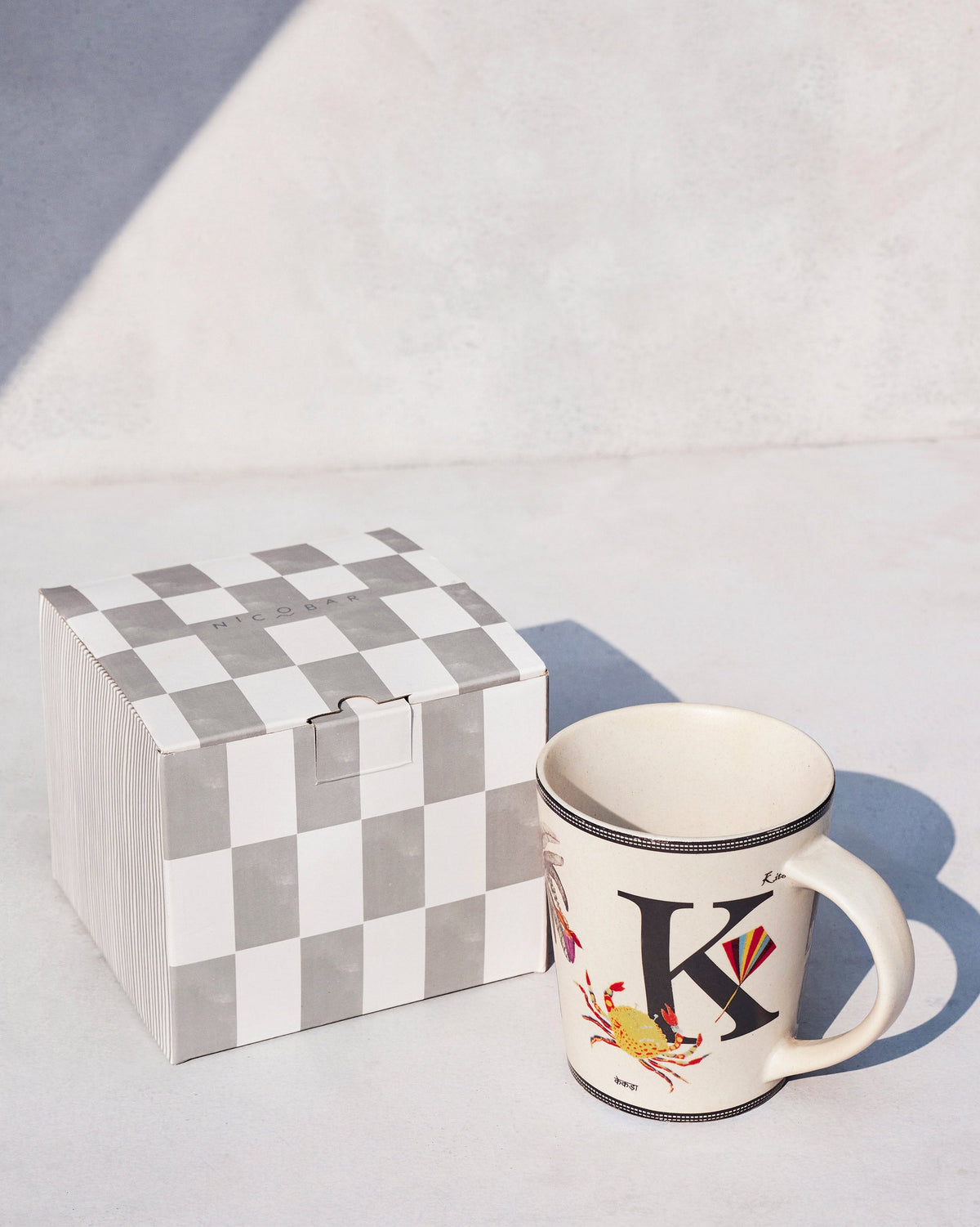 Cream Kamal mug with letter K beside a Nicobar gift box.