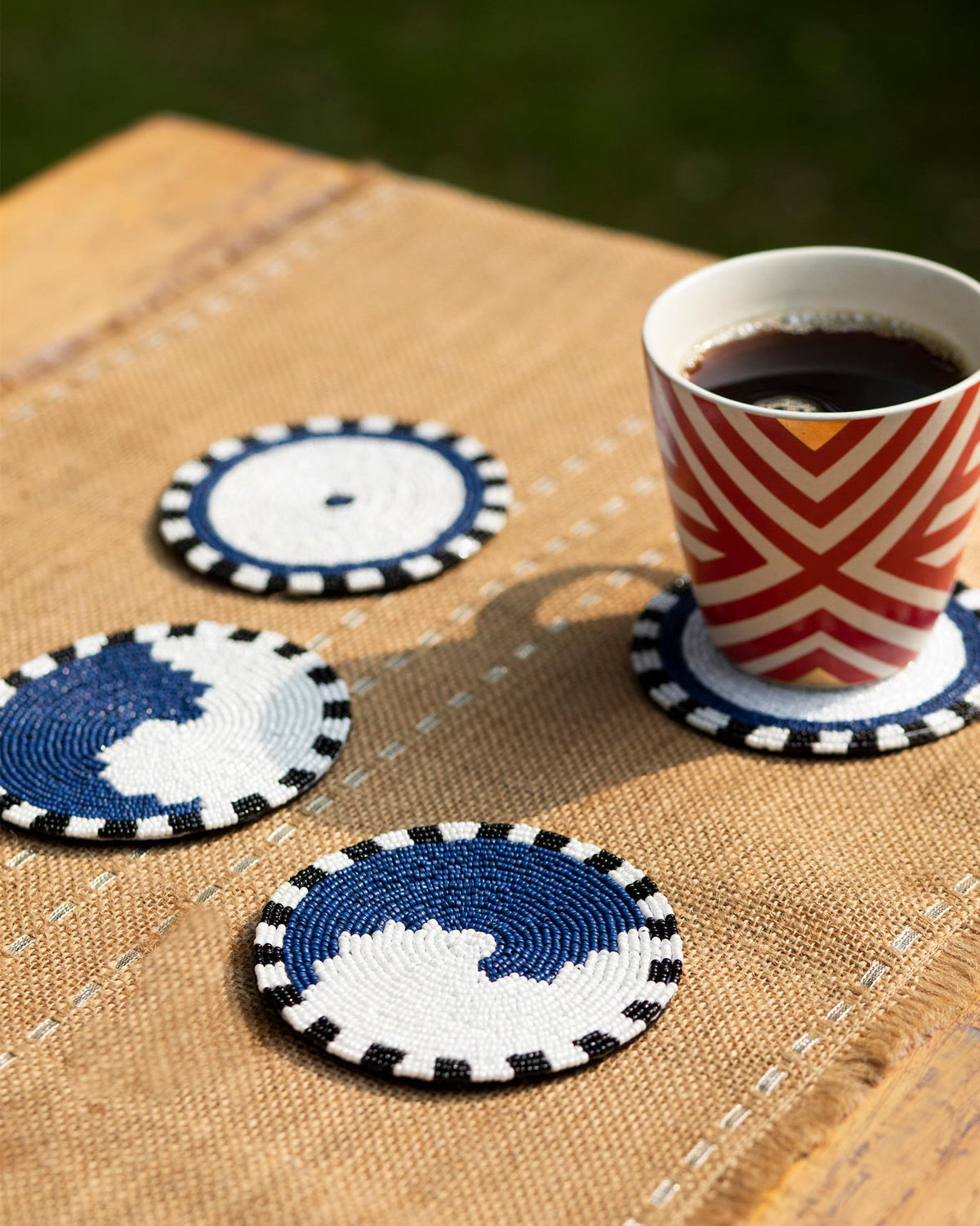 Three Dhaara Coasters with blue and white beaded designs on a jute table.
