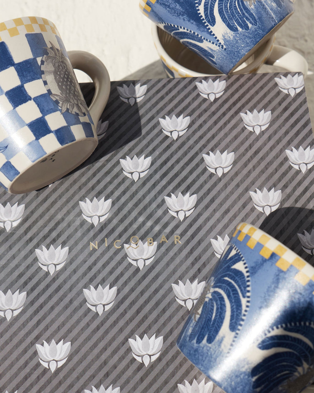 Bodhi Espresso Mugs with blue checks and palm motifs, set on a patterned surface.