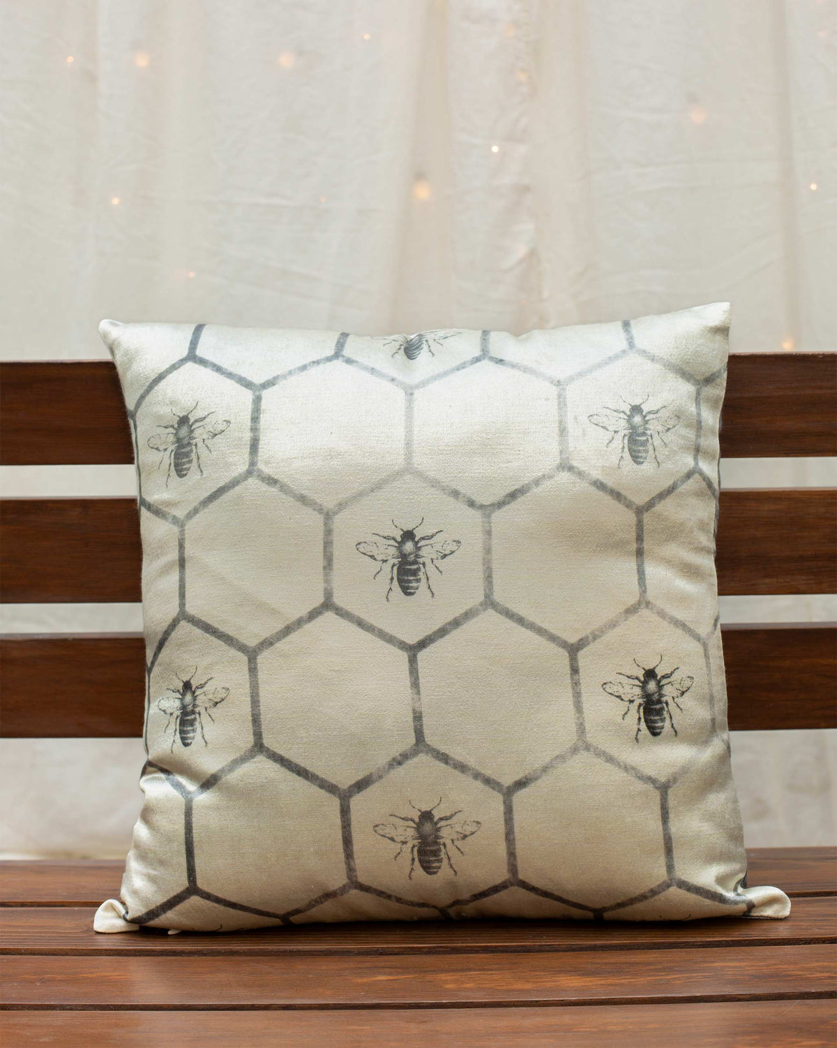 Cushion in cream with a grey honeycomb pattern and bees on a wooden bench.