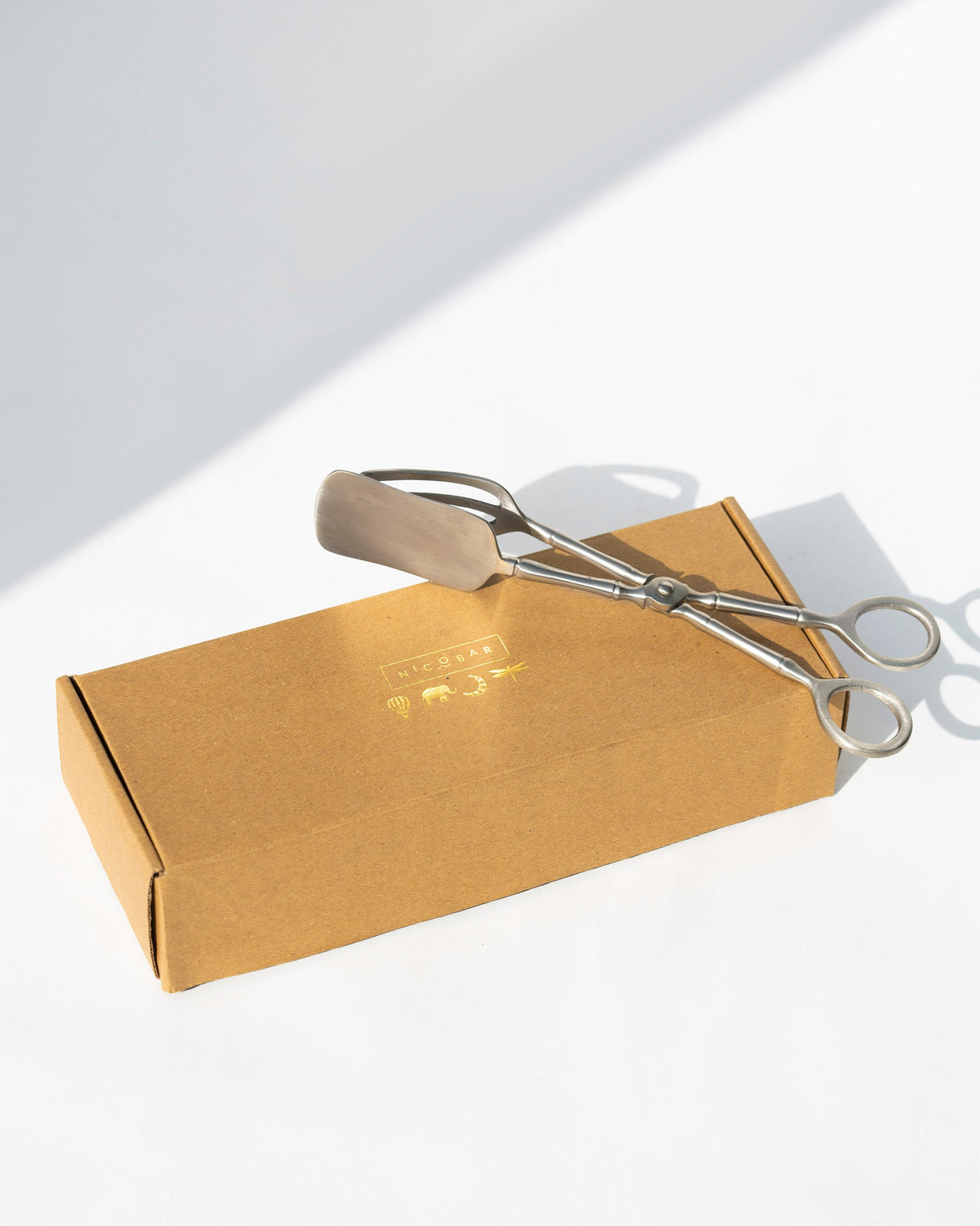 Celeste Dessert Server tongs resting on a brown gift box.