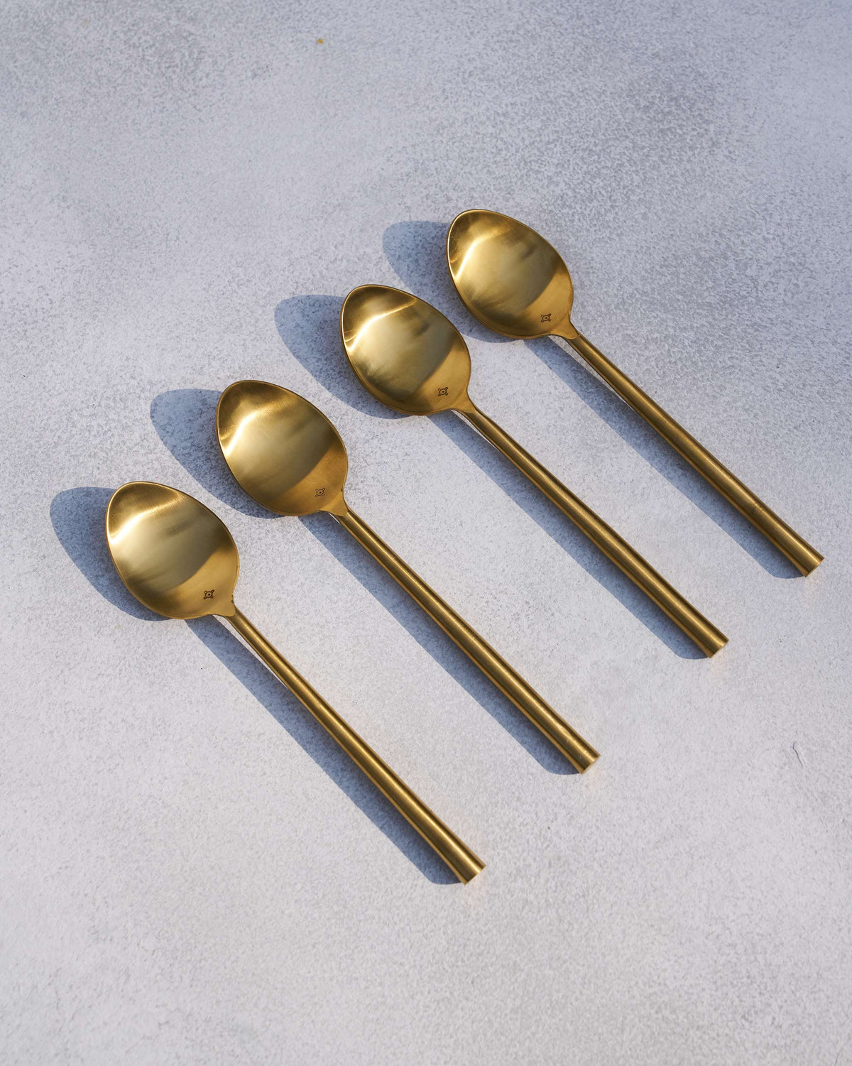 Four brass spoons laid out diagonally on a grey surface.