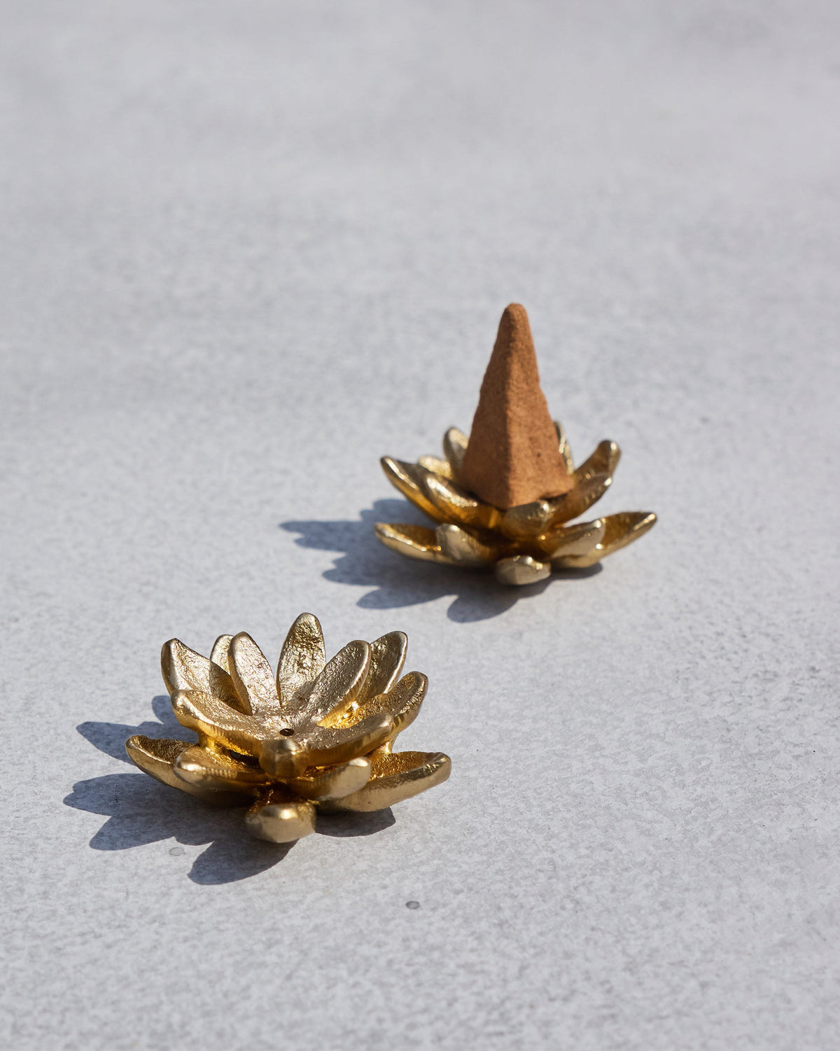 Kamal gold lotus incense holders, one empty and one with a cone.