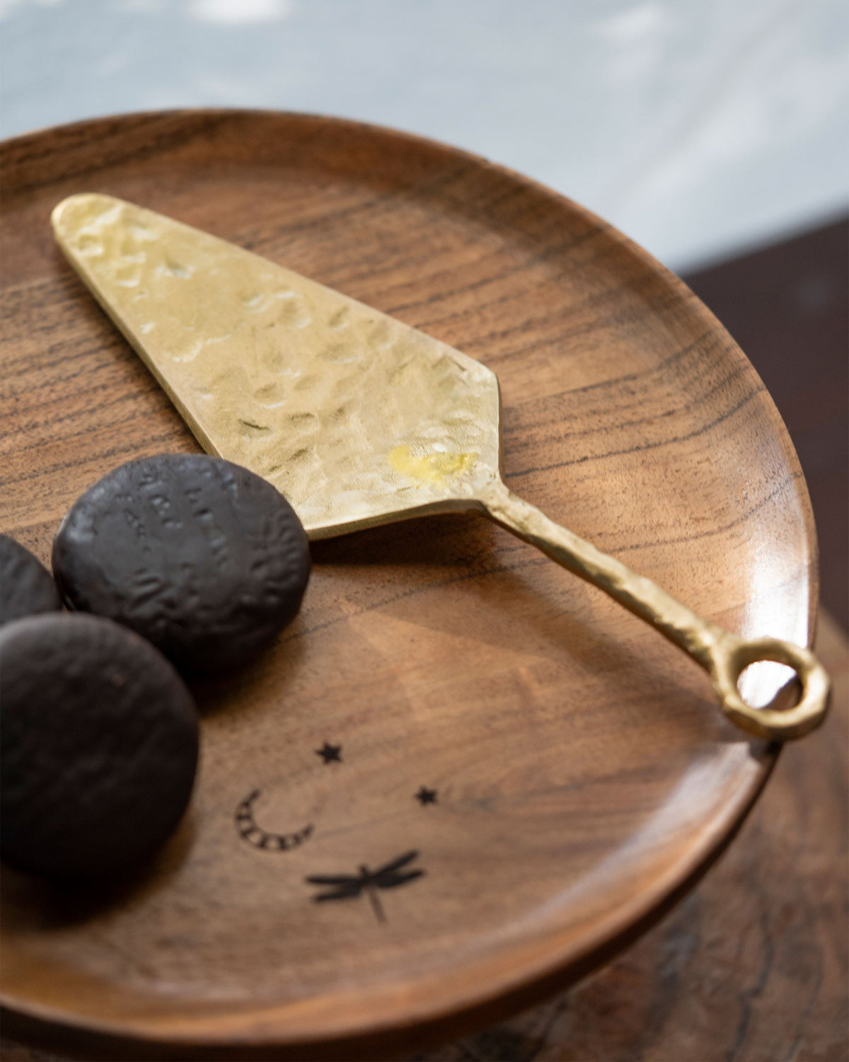 Angled view of Celeste Spatula on a wooden plate beside dark cookies.