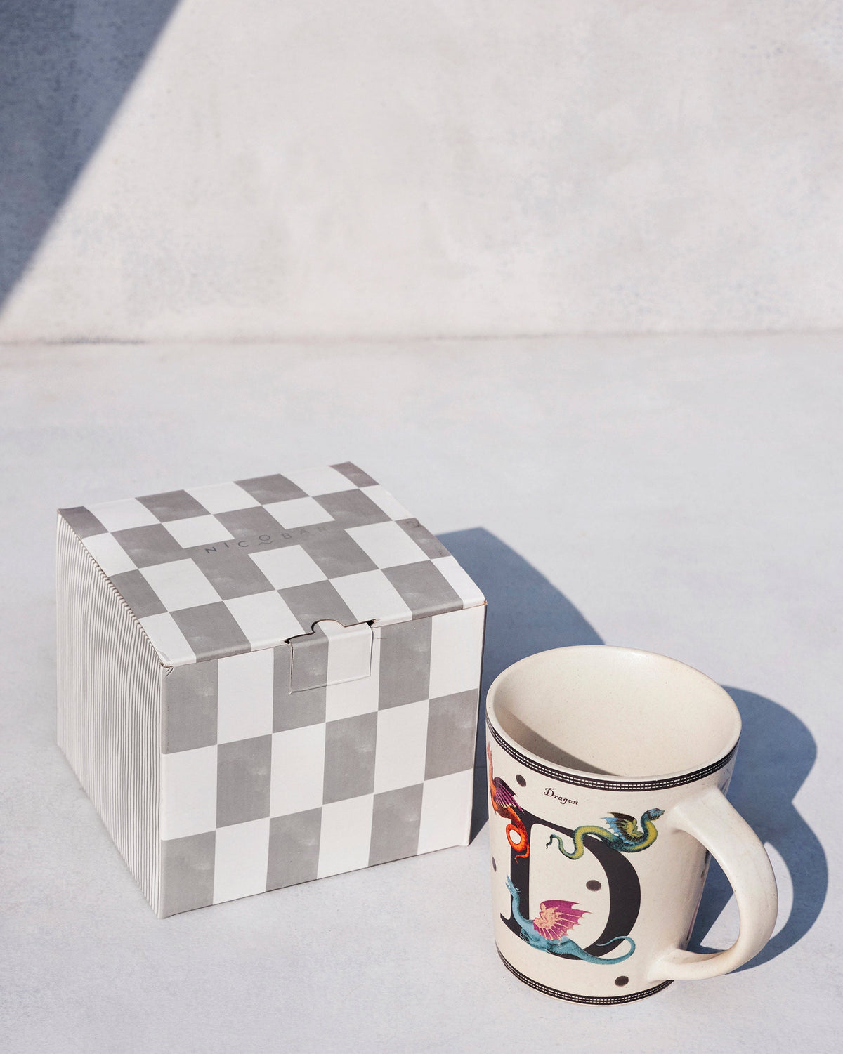 Cream Dariya mug with dragon motifs beside a grey checkered gift box.